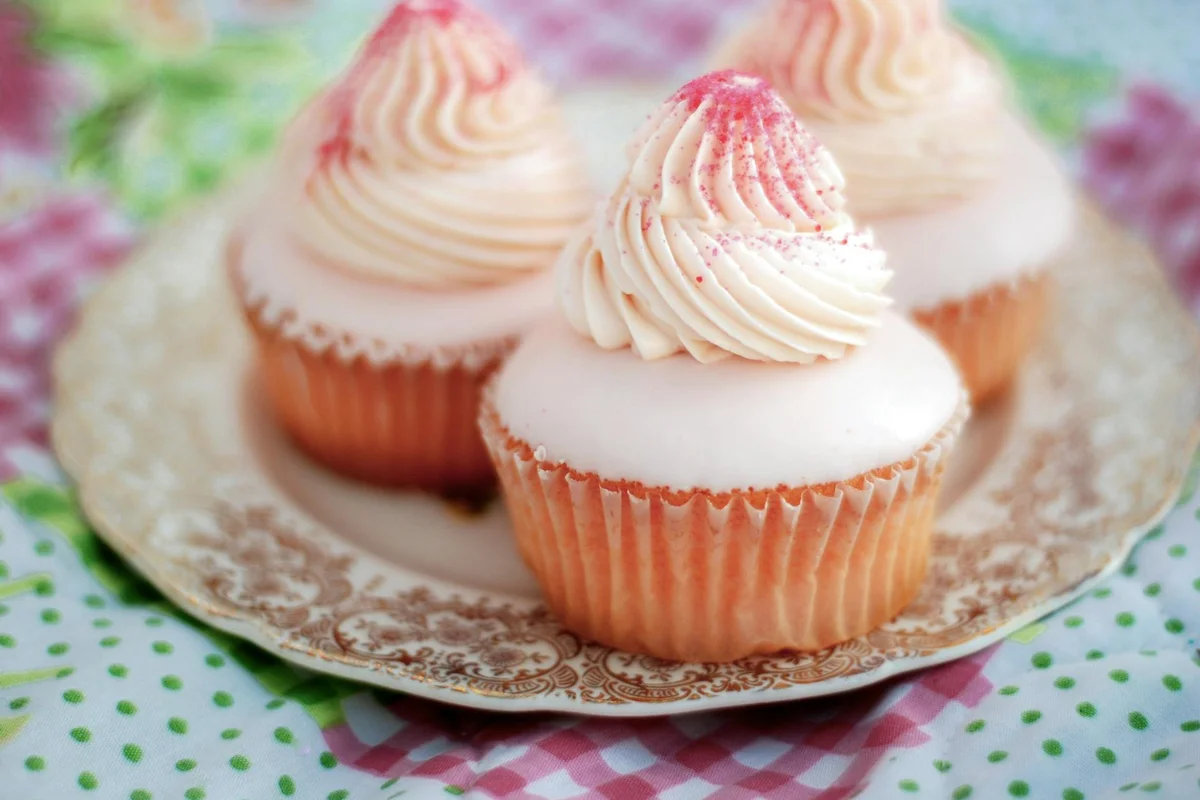 Smiling woman with a towel wrapped around her head, applying foamy face wash in a bathroom.