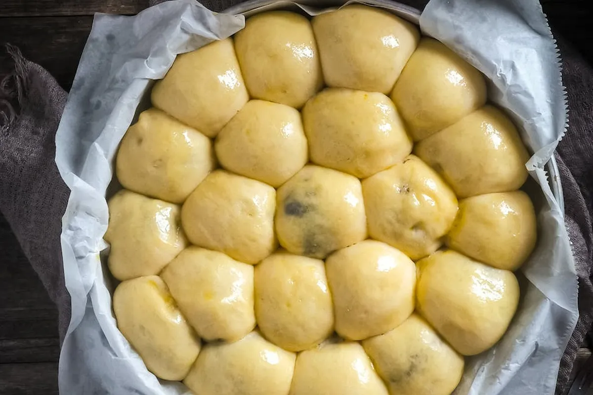 Smiling woman with a towel wrapped around her head, applying foamy face wash in a bathroom.